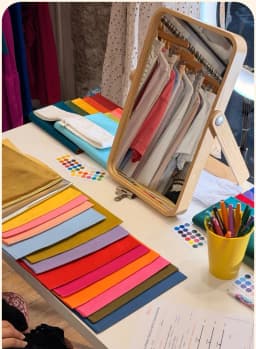 Atelier colorimétrie : nuancier de bandes de tissu colorées déployées sur une table devant un miroir en bois