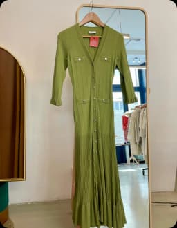 Robe longue en maille verte, boutonnée sur l'avant, suspendue devant le grand miroir de la boutique